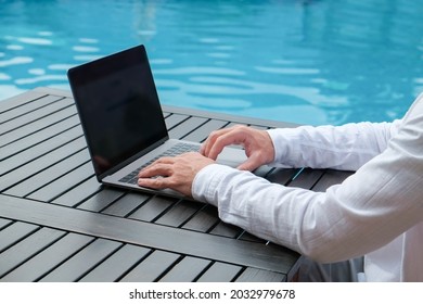 Young Man Wearing White Linen Shirt Working On His Laptop By The Pool. Male Travel Blogger Typing On Keyboard. Perks Of Being A Freelancer. Close Up, Copy Space, Background.