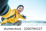 Young man wearing winter clothes taking selfie picture in winter snow mountain - Happy guy with backpack hiking outside - Recreation, sport and people concept