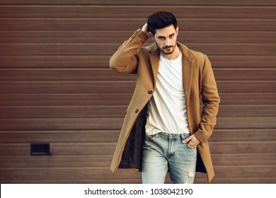 Young man wearing winter clothes in the street. Young bearded guy with modern hairstyle with coat, blue jeans and white t-shirt. - Powered by Shutterstock