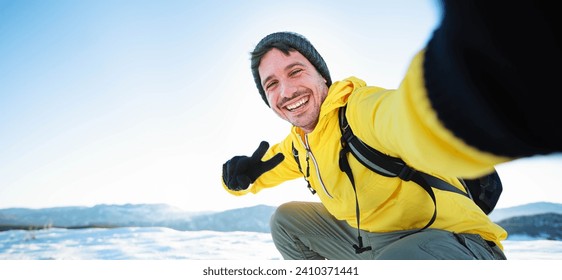 Young man wearing winter clothes taking selfie picture in winter snow mountain - Happy guy with backpack hiking outside - Recreation, sport and people concept - Powered by Shutterstock