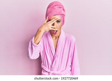 Young Man Wearing Woman Make Up Wearing Shower Towel On Head And Bathrobe Peeking In Shock Covering Face And Eyes With Hand, Looking Through Fingers With Embarrassed Expression. 