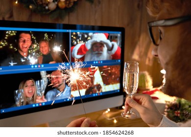 Young man wears Christmas hat drinking champagne holding sparkler talking to friends on virtual video call celebrate Happy New Year party in distance online chat at home, over shoulder screen view.