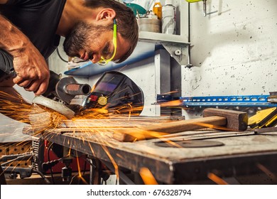 A young man welder a brunette in a black T-shirt and safety goggles. He processes a metal item from a angle grinder in the workshop. Close-up on the sides fly sparks from the  a angle grinder - Powered by Shutterstock