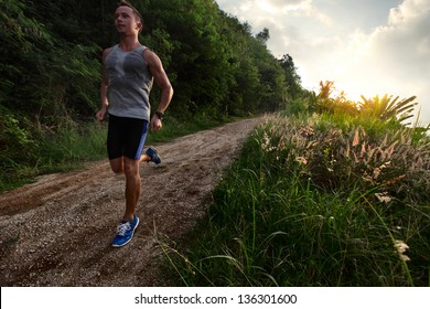 Young man with wet singlet running on a rural road during sunset