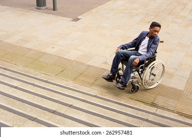 young man in a wheelchair at the bottom of a staircase unable to continue.