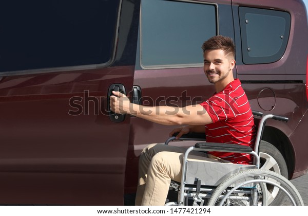 Young\
man in wheelchair opening door of his van\
outdoors