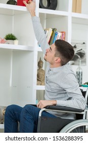 Young Man In Wheelchair Reaching For Object From High Shelf