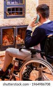 Young man in a wheelchair talking on his cell phone next to a wood-burning fireplace.
