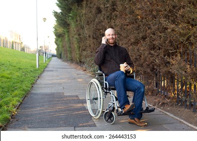 Young Man In A Wheelchair Talking On The Phone With A Coffee