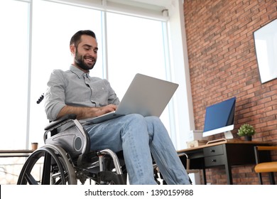 Young Man In Wheelchair Using Laptop At Office