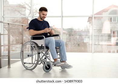 Young man in wheelchair using mobile phone near window indoors - Powered by Shutterstock