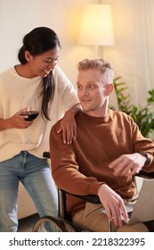 Young Man In Wheelchair Working On Laptop When His Wife Drinking Glas Of Red Wine