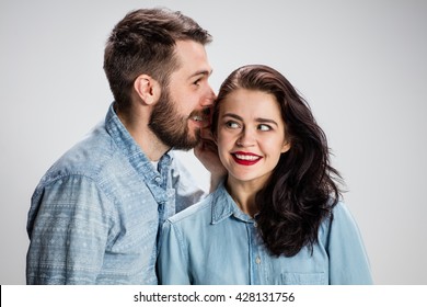 Young man whispering to woman (girlfriend) - indoor lifestyle photo on gray background