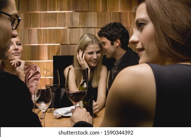 Young Man Whispering In Woman's Ear At Party