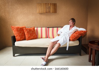 Young Man In White Bathrobe Sitting On The Couch Relaxing With A Glass Of Whiskey