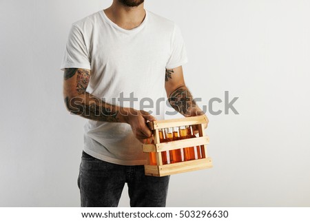Young man in white cotton t-shirt with tattoos holding a crate of artisan beer isolated on white