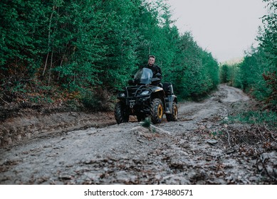 A Young Man In A White Helmet Rides Through The Woods On A Quad Bike. Extreme Hobby. A Trip To ATV On The Road From Logs. Quad Biking Through The Forest.