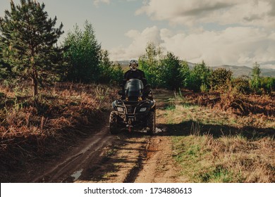 A Young Man In A White Helmet Rides Through The Woods On A Quad Bike. Extreme Hobby. A Trip To ATV On The Road From Logs. Quad Biking Through The Forest.