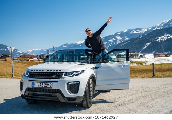 Young man, White Range Rover Evoque. Austria, Alps -\
March 25, 2018: Latest brand new white 2018 Range Rover Evoque. Man\
standing by the car.