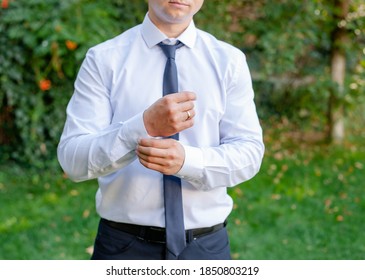 A young man in a white shirt and tie straightens his cufflinks on his sleeves. Official dresscode