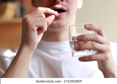 young man in a white T-shirt drinks a capsule for treatment with water