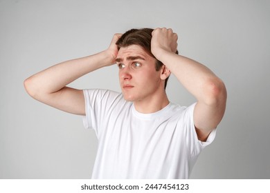 Young Man In White T-Shirt Looking Worried With Hands On Head Against Plain Background - Powered by Shutterstock