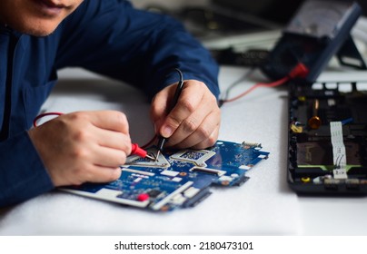 young man who is a computer technician A laptop motherboard repairman is using an IC meter to look for defects on the motherboard to repair on his desk. Board repair with modern technology - Shutterstock ID 2180473101