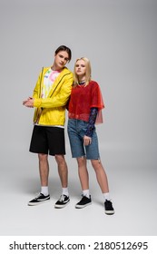 Young Man In Windbreaker Standing Near Blonde Girlfriend On Grey Background