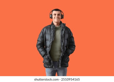 Young man in winter clothes with headphones on orange background - Powered by Shutterstock