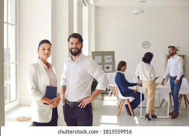 Young Man And Woman, 2 Successful Company Co-founders, Business Partners Or Coworkers Looking At Camera. Confident Female Executive Director And Male Manager Standing In Office After Corporate Meeting