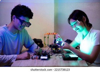 Young Man And Young Woman Amateur Inventor Testing Electronic Device Model Inventions All Wear Vr Glasses To Show High Technology In Black Light Mood.