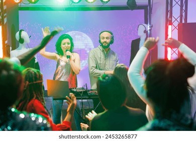 Young man and woman band performing on stage in nightclub at techno music festival. People partying on dancefloor while enjoying singer and dj playing at live concert in club - Powered by Shutterstock