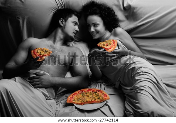 ベッドの若い男性と若い女性がピザを手にして の写真素材 今すぐ編集