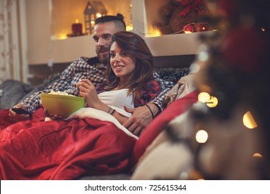 Young man and woman in bed watching tv and eating pop corn