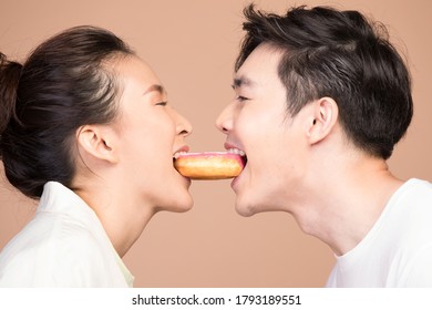 Young Man And Woman Biting Donut Together From Opposite Side