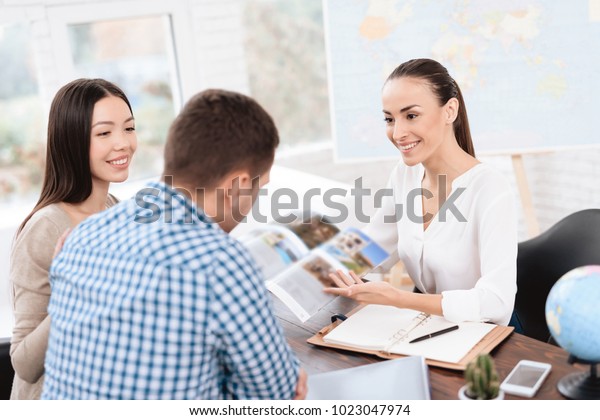 A young man and a\
woman came to the travel agency. They want to go on a trip during\
their holidays. The girl agent offers them different countries. She\
shows it in the booklet.