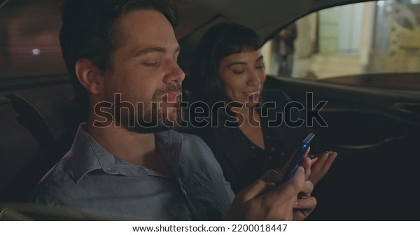 Young man and woman in car\
backseat talking and smiling. Male colleague showing smartphone\
device screen to friend in cab transportation. People in commute\
after work