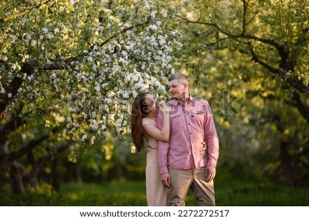 Young man and woman couple in a blooming apple garden. Tender holding each other. Spring lovestory. Brown-haired girl with long hairs and man in pink shirt. Young family. Couple romantic spring date