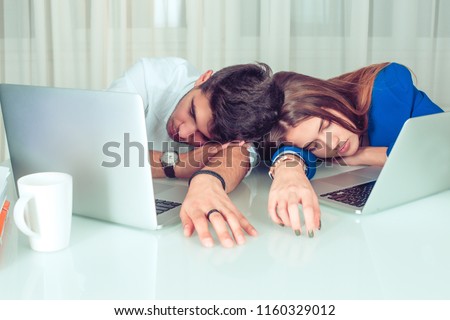 Young man and woman couple colleagues lying on table with laptops and sleeping in laziness and procrastination in office sleeping. Overworking, late hours, night shift, sleepless, lazy workers concept