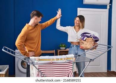 Young Man And Woman Couple Hanging Clothes On Clothespin High Five At Laundry Room