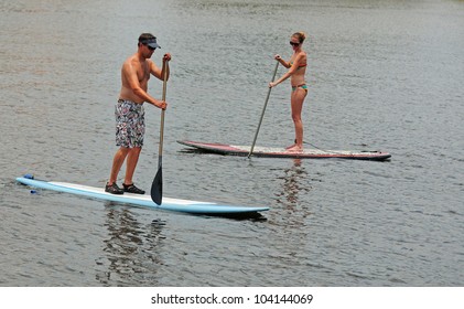 Young Man And Woman Couple Paddle Boarding In Ocean