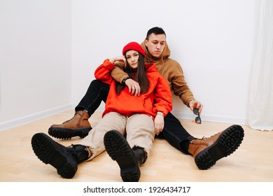 Young Man And Woman Cuddling, Sitting On The Floor In Hoodies And Army Boots. High Quality Photo