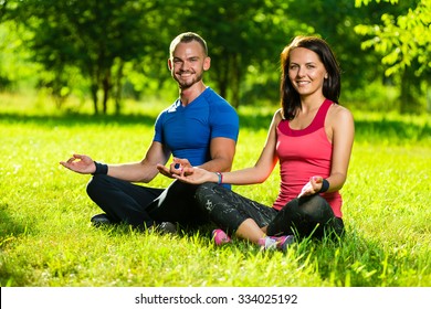 Young Man And Woman Doing Yoga In The Sunny Summer Park. Couples Yoga On Green Grass Outdoor.