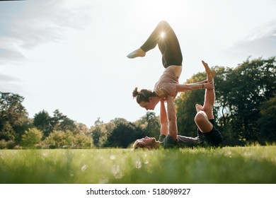 Young man and woman doing yoga in pair outdoors. Couple doing acro yoga in park. - Powered by Shutterstock