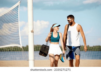 Young man and woman going to play tennis on beach on warm summer day. Sportive young people in sportswear carrying tennis equipment. Concept of sport, leisure time, active lifestyle, game, summertime - Powered by Shutterstock