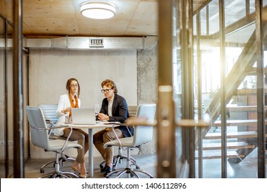 Young Man And Woman Having A Business Conversation During The Small Conference, Sitting At The Round Table In The Meeting Room