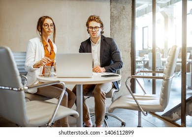 Young Man And Woman Having A Business Conversation During The Small Conference, Sitting At The Round Table In The Meeting Room