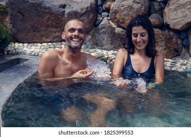 Young man and woman having recreational bath in the water filled with ice cubes. Multiethnic couple getting cryo therapy outdoors