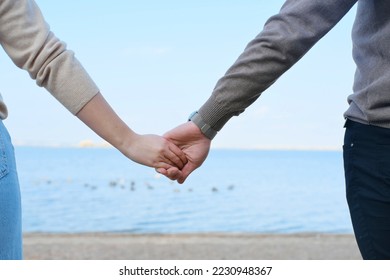 Young man and woman hold hands against the backdrop of blue water and sky. Close-up of hands. Horizontal photo - Powered by Shutterstock