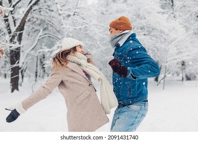Young man and woman jumping and tossing snow up in winter park. Couple having fun playing outdoors